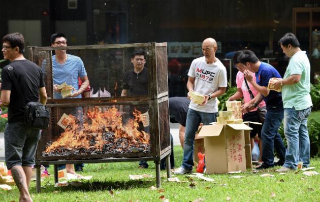 Employees from a nearby office building burn offerings to mark the Hungry Ghost Festival in Singapore on August 8, 2014. Superstition comes to the fore during the month-long Hungry Ghost Festival, which traditionally begins this time of year. Chinese superstition holds that the gates of hell are opened for spirits to wander across the mortal realm before they return to the underworld. AFP PHOTO / ROSLAN RAHMAN